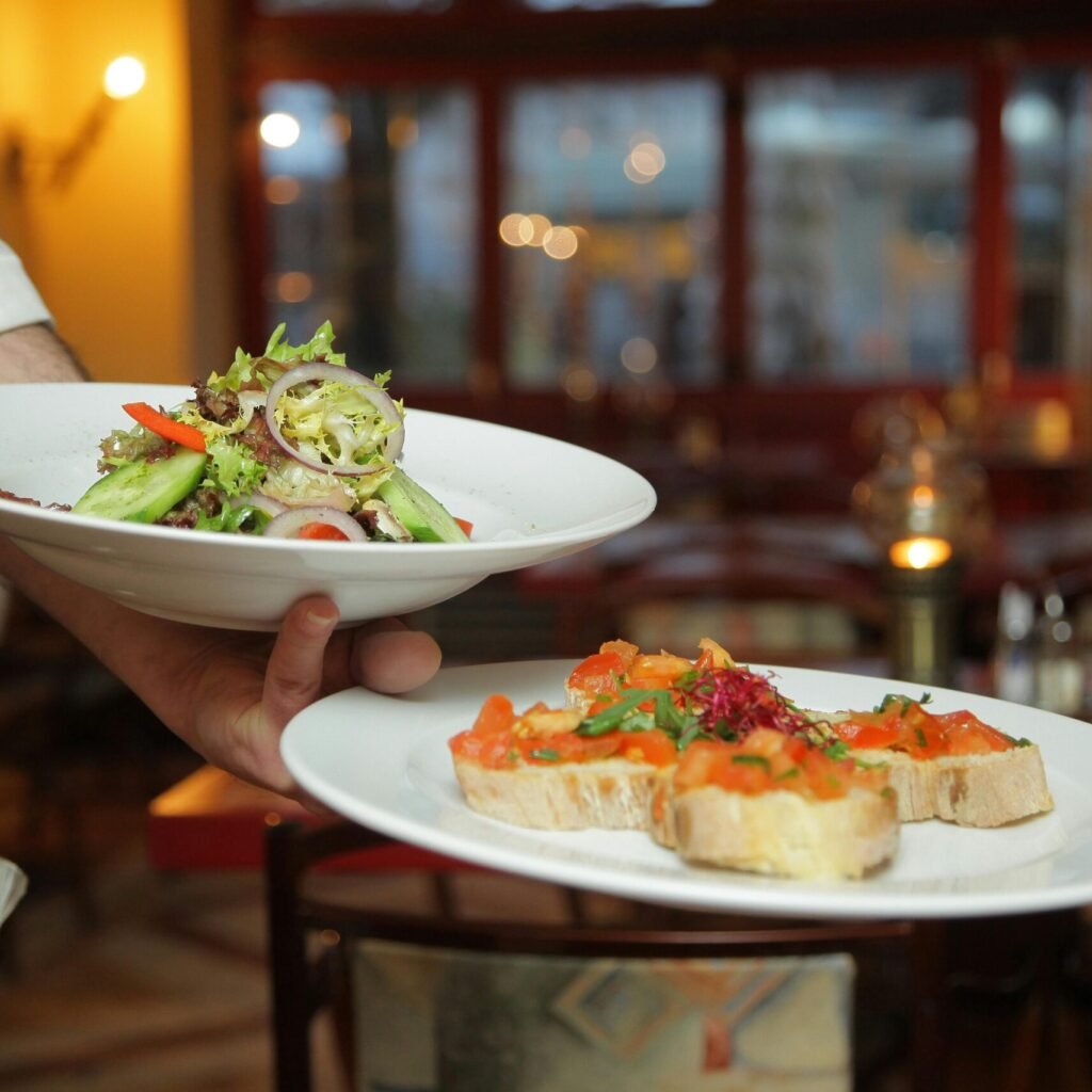 A waiter serves a fresh salad and hors d'oeuvres in a cozy restaurant setting.