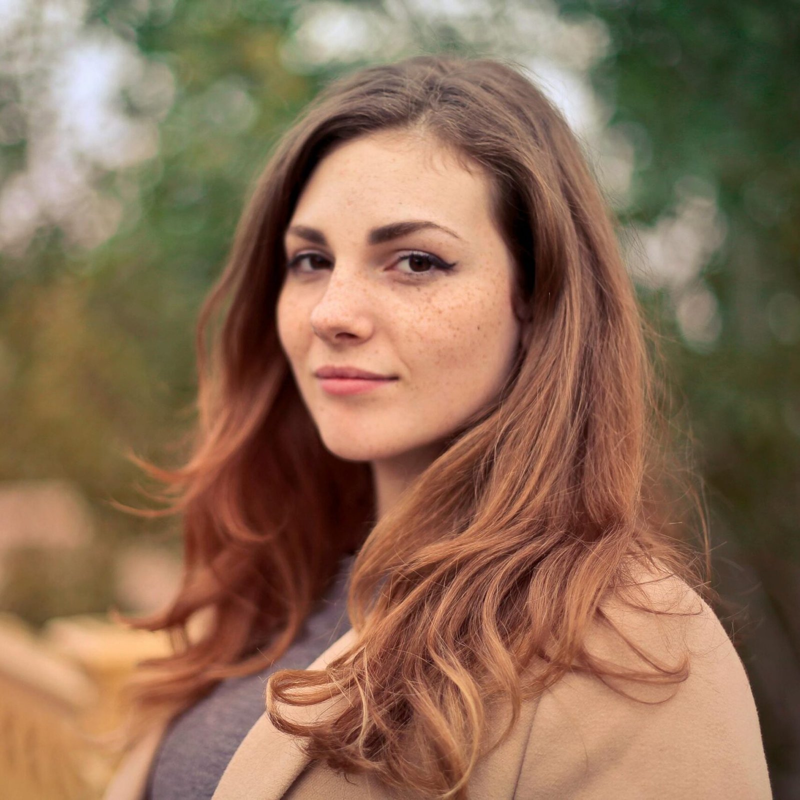 A young woman with long hair smiles confidently for an outdoor portrait session.